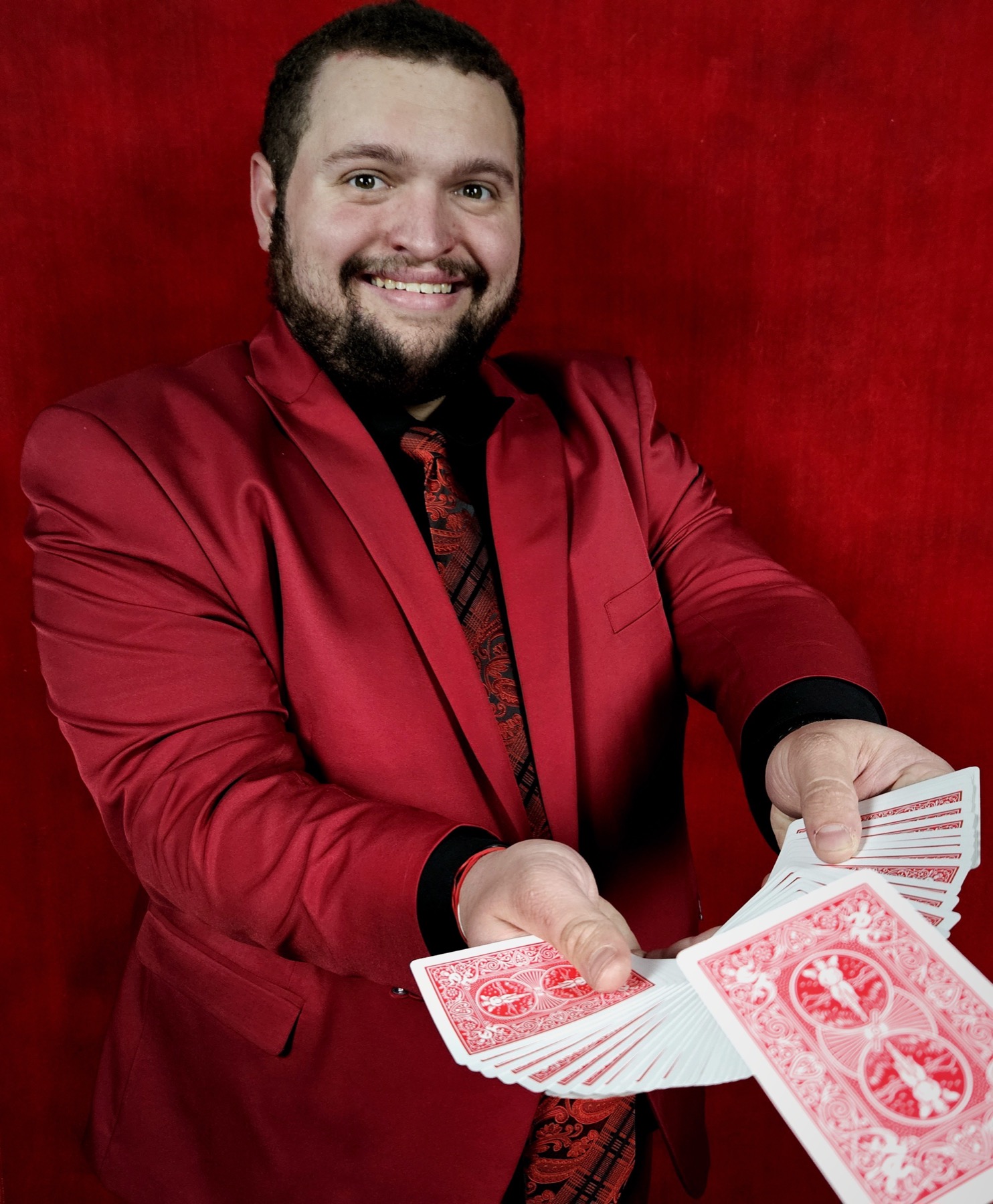 Bryce smiling in a red jacket while flourishing a deck of cards